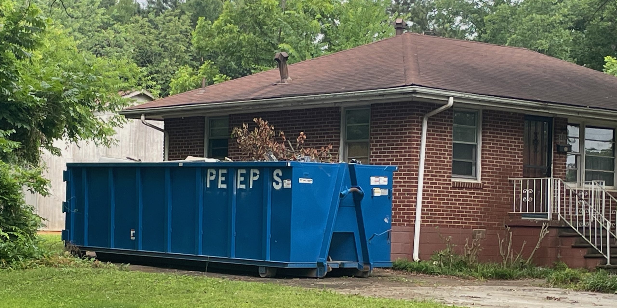 30 yard Forest park clean out Blue dumpster in a residential driveway beside a brick house with a brown roof and green trees in the yard.
