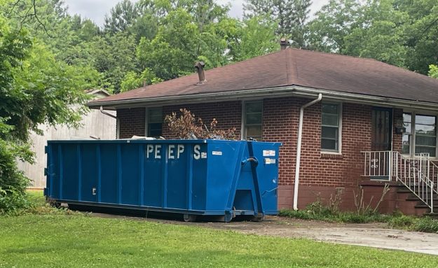 30 yard Forest park clean out Blue dumpster in a residential driveway beside a brick house with a brown roof and green trees in the yard.