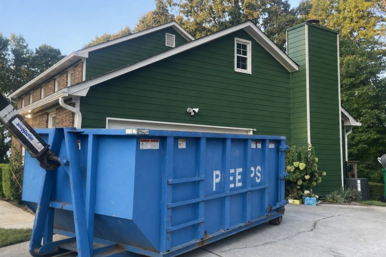 dumpster-rental-prices-atlanta-peeps-containers Blue dumpster on a driveway in front of a green house with white trim.